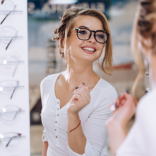 A woman tries on eyeglasses in front of a mirror.